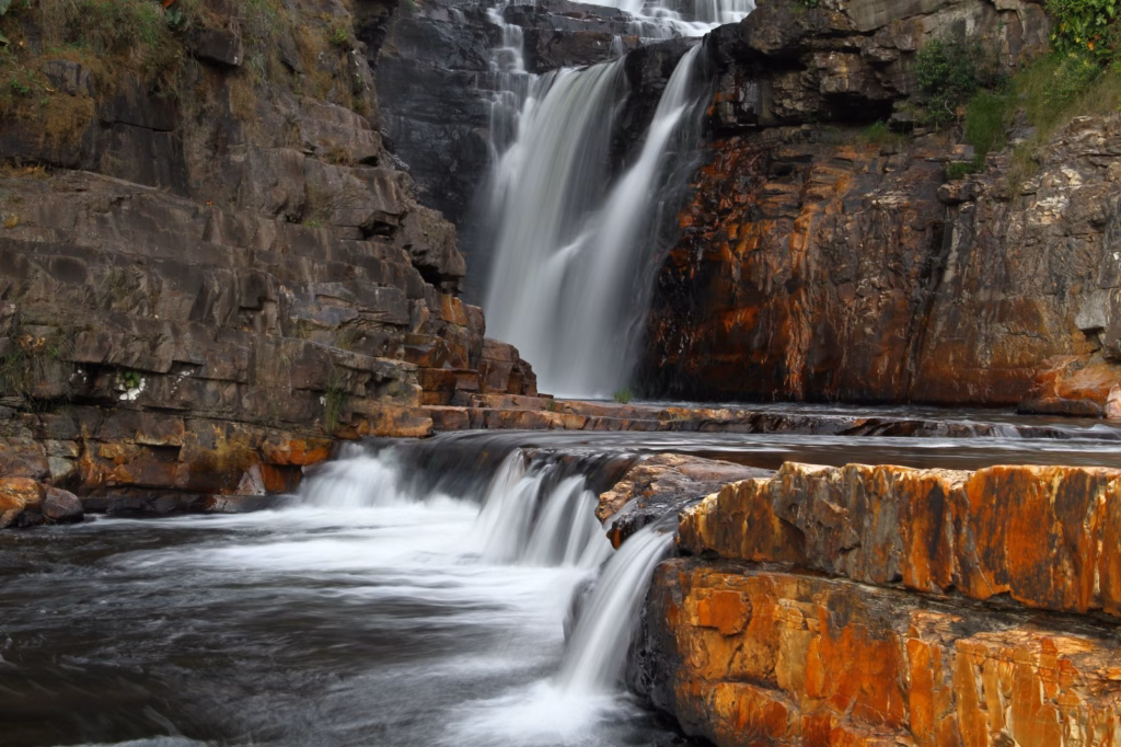 Cachoeira do Parafuso - Catarata dos Couros na Chapada dos Veadeiros. Água fluindo em cascata entre paredões de pedra e degraus rochosos de tons alaranjados com efeito de longa exposição.