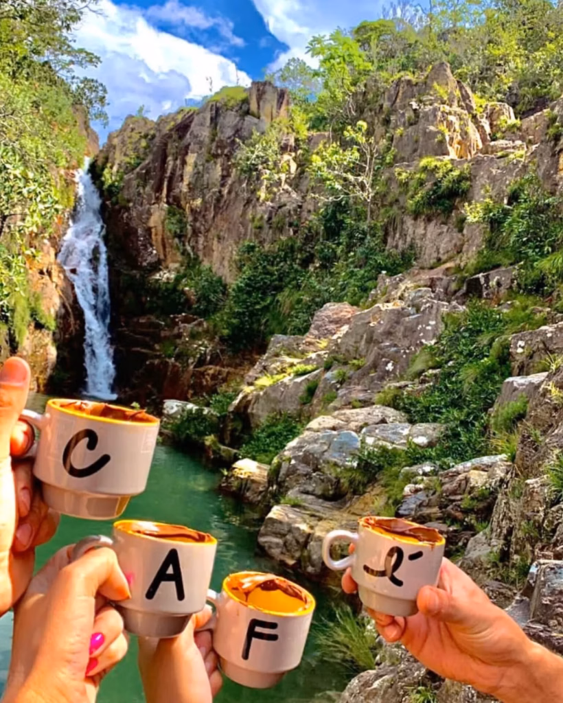 Brinde com xícaras de café personalizadas com letras diante de uma paisagem natural com cachoeira na Chapada dos Veadeiros