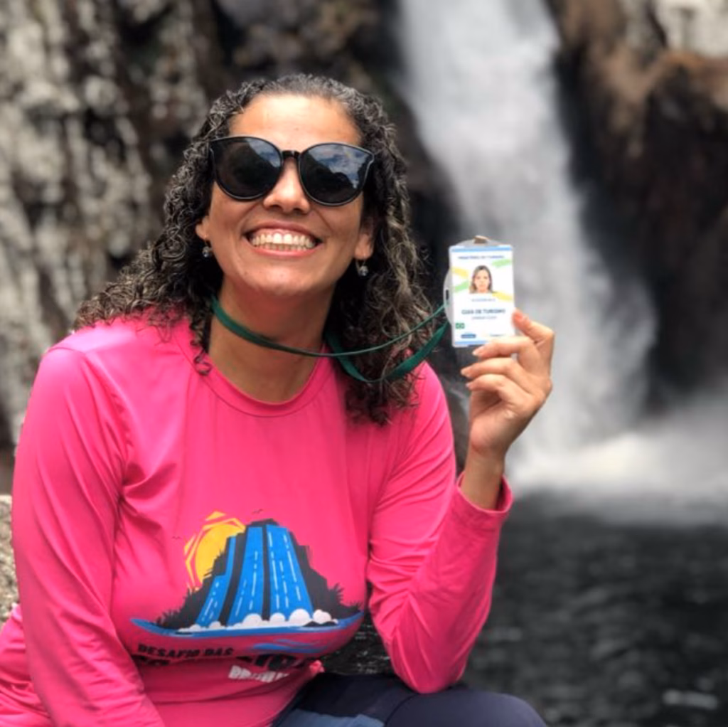 Guia de Turismo da Chapada dos Veadeiros: Janna Guia segurando a carteirinha de guia nacional de frente a uma cachoeira