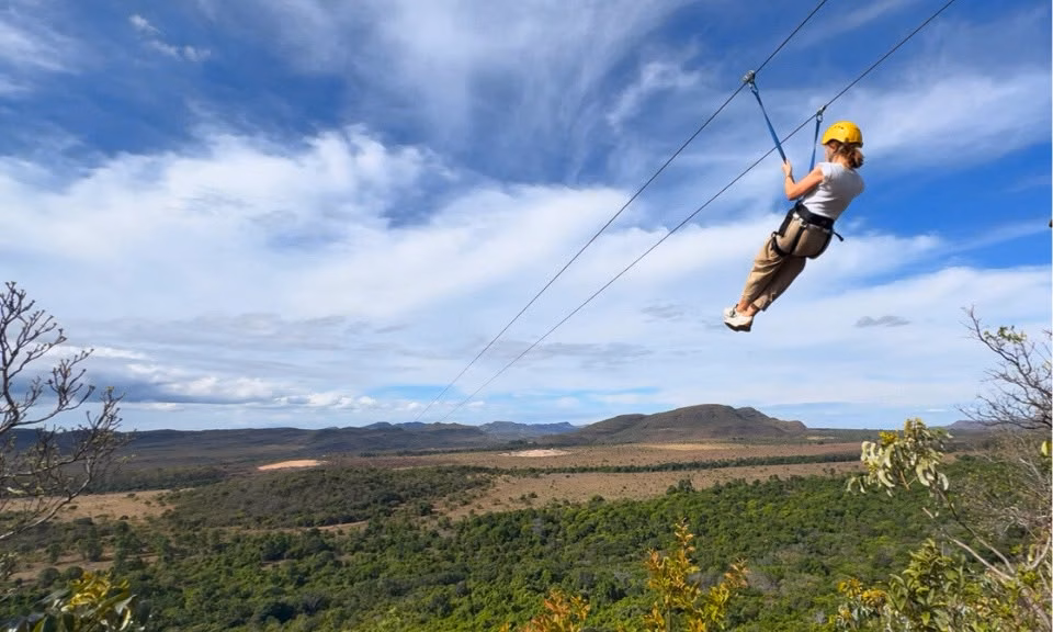 Rapaz descendo a Tirolesa do Gavião, na Fazenda São Bento, em Alto Paraíso de Goiás, com vista para o Cerrado e as paisagens da Chapada dos Veadeiros. Uma das principais atrações de aventura da região.
