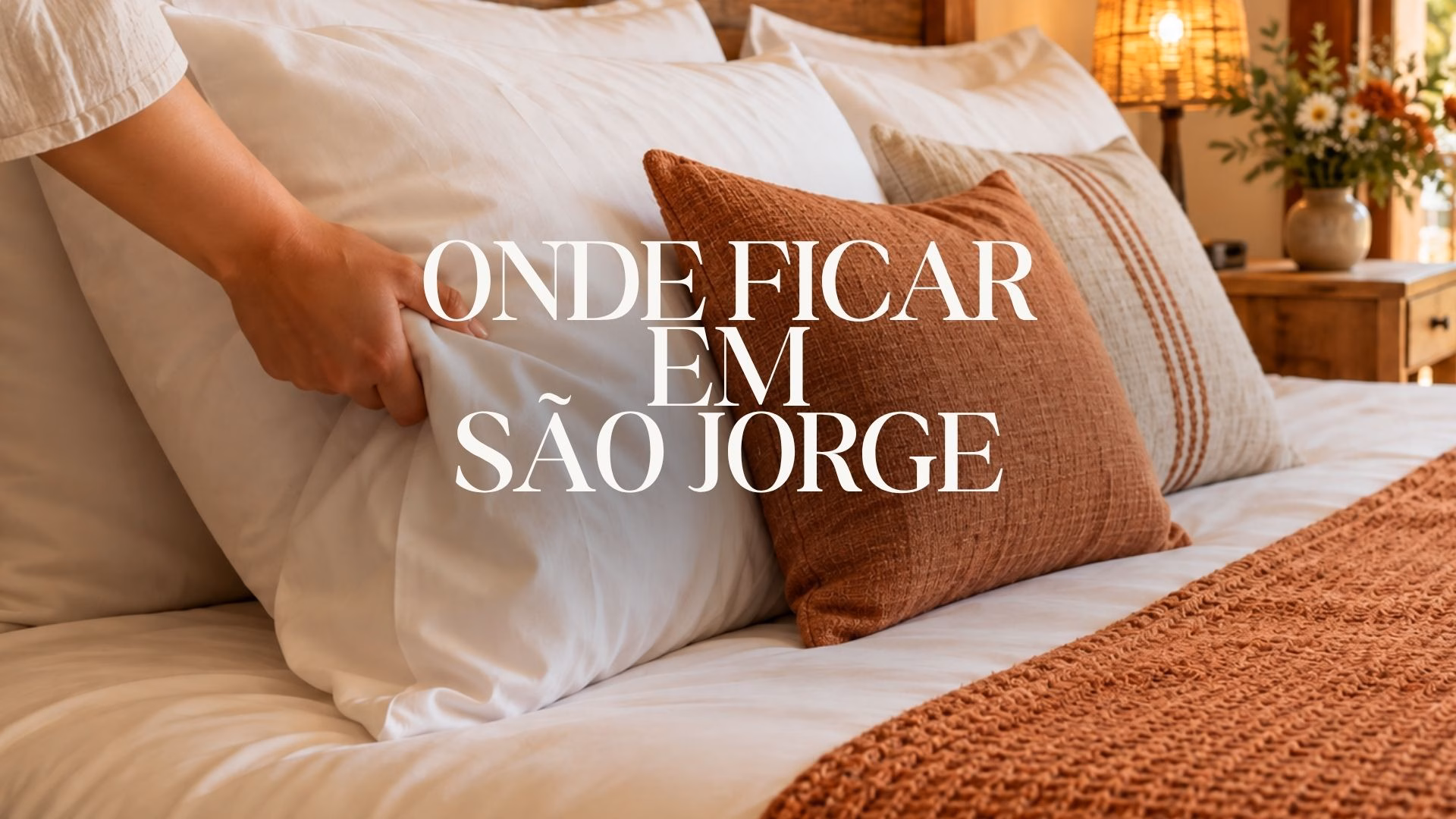 Imagem ilustrativa de cama aconchegante com almofadas terracota e decoração rústica, com o título “Onde ficar em São Jorge”.