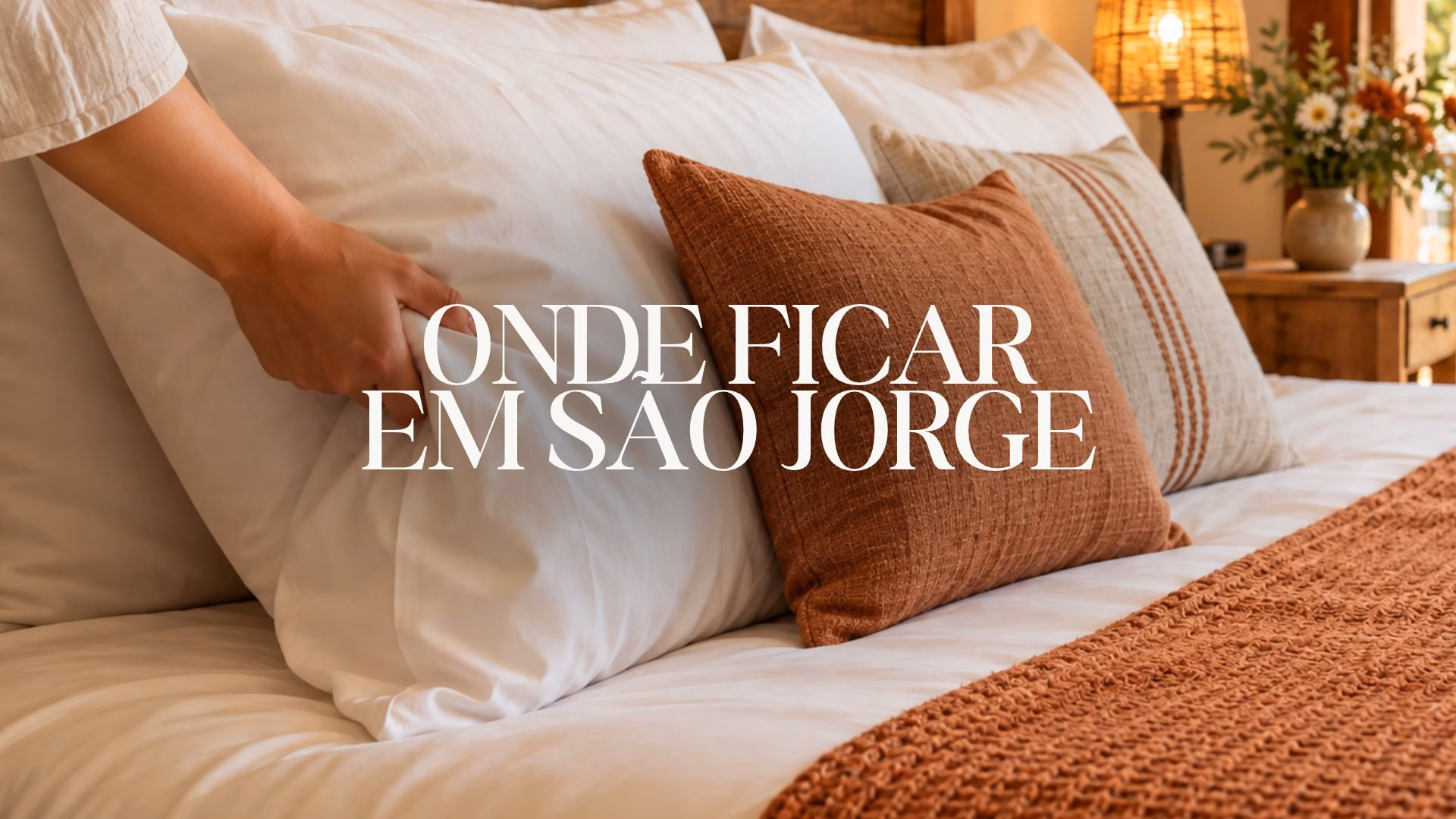 Imagem ilustrativa de cama aconchegante com almofadas terracota e decoração rústica, com o título “Onde ficar em São Jorge”.